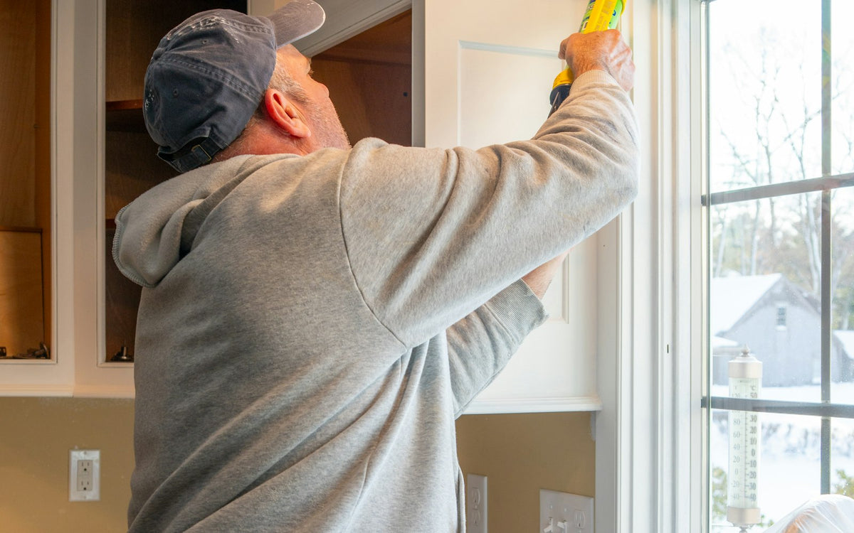 Person applying silicone caulk with a caulking gun along a kitchen window frame - EQUIPE Egypt